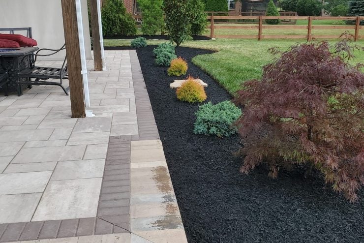 358389378_741700687761102_6153874435248790698_n Landscaped backyard with a paved patio, mulched planting beds, shrubs, lawn, and a wooden fence