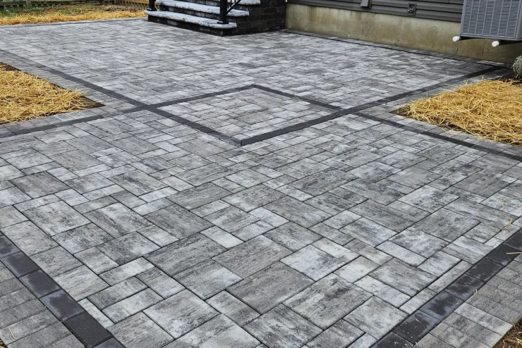 Cincinnati_Landscapedesigner_landscapeconsultation_LeonsLandscaping (42) Gray interlocking paver patio with dark edging beside a house and landscaped beds