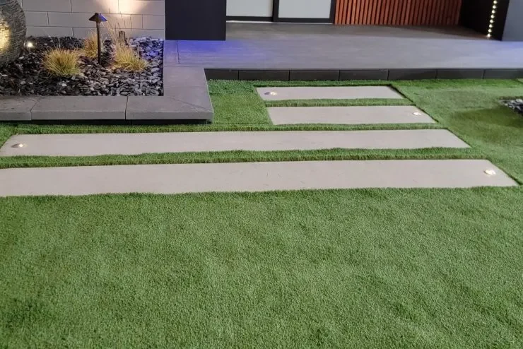Cincinnati_Landscapedesigner_landscapeconsultation_LeonsLandscaping.webp (9) Landscaped yard with artificial grass, concrete stepping paths, a rock garden, and outdoor lighting